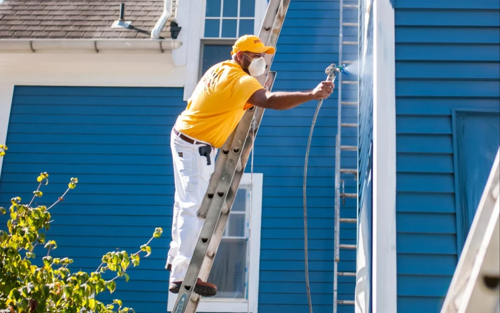 a man on a ladder spraying a wall